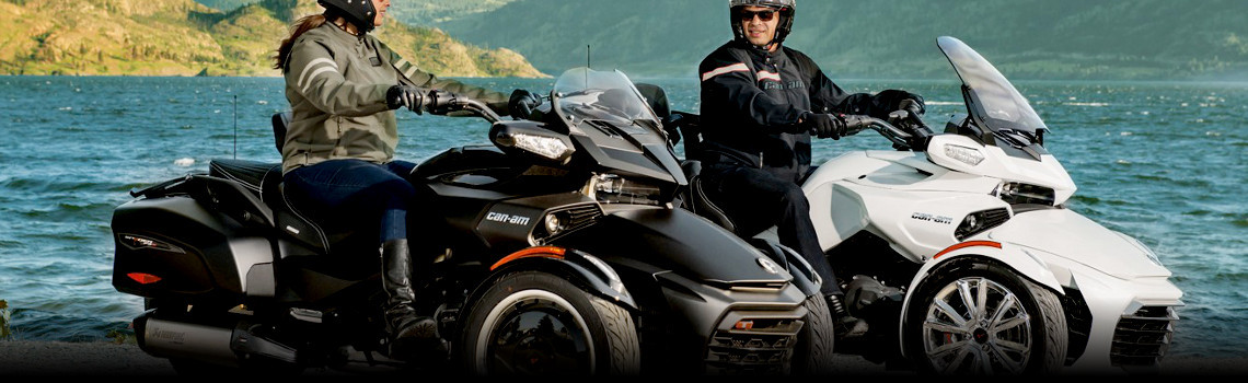 Two people on Can-Am® Spyder® F3 trikes parked beside the coast